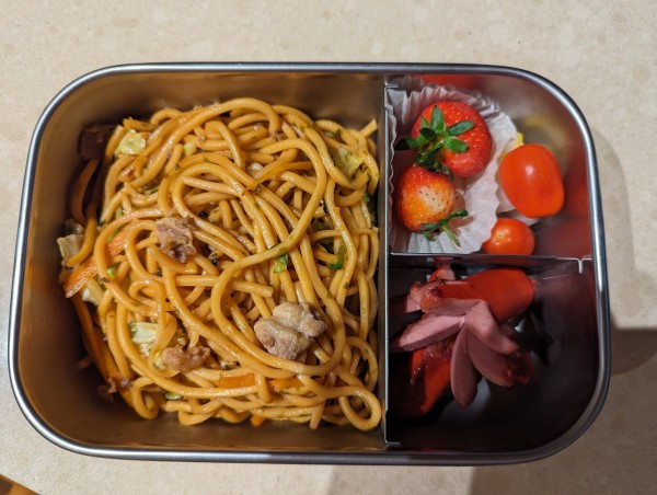 A bento box for school containing yakisoba noodles, octopus Frankfurts, strawberries, cherry tomatoes,.daikon