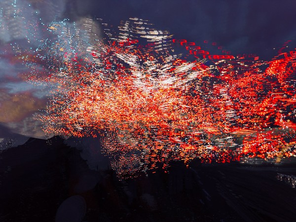 This image is an urban landscape photograph using glitchy generative techniques to paint an abstract expressionist and dynamic chaos of coloured lights, predominantly orange fiery reds across a dark blue purple and black backdrop. 