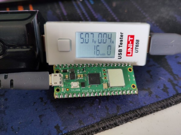 Raspberry Pi Pico placed alongside an UT658 power meter. The Pico is connected to the power meter with a grey cable. The power meter is connected to a powerbank. The Pico is powered from the powerbank via the power meter, so that the power usage can be monitored.