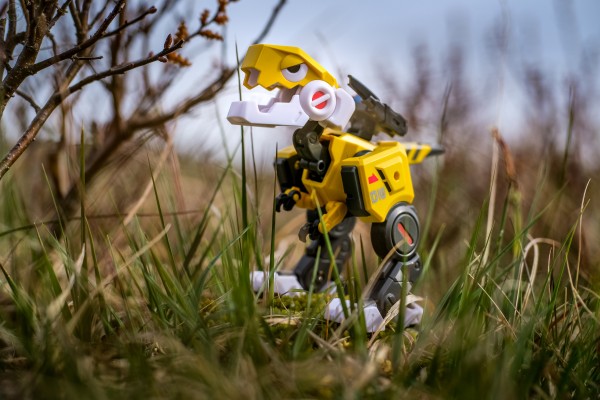 Yellow robot raptor toy shot among grass and bushes