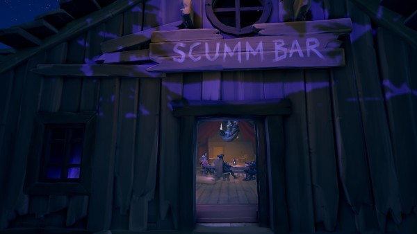 The exterior of a wooden building named "SCUMM BAR" at nighttime, with a glimpse through the open doorway revealing people seated at tables inside.