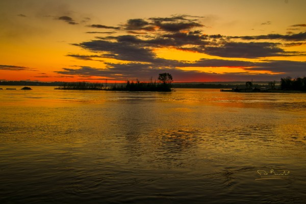 Photograph of a vibrant sunrise over St. Mary's River in Sault Ste. Marie, Michigan, showcasing fiery orange and yellow skies reflected in the rippling waters. Image at:  https://beautifulsunphotography.com/featured/dawns-first-light-on-the-st-marys-river-deb-beausoleil.html See more art & blog at: https://beautifulsunphotography.com/ https://debbeautifulsunphotography.com/ https://www.zazzle.com/store/beautifulsun_designs https://debbeausoleil.com