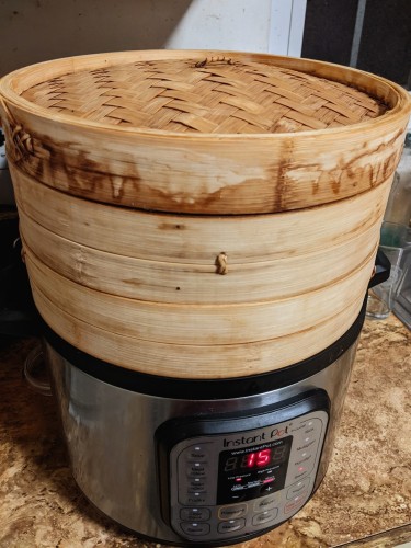 Bamboo steamer basket with lid over an instant pot set to steam