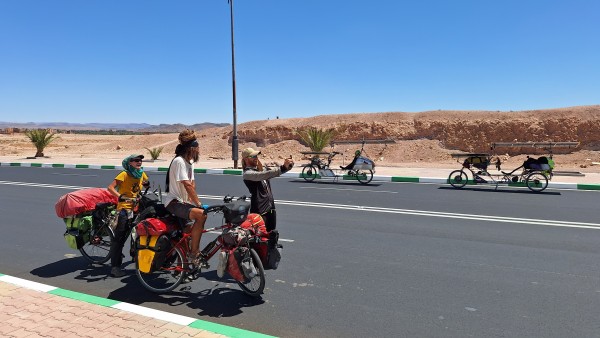 Pair of heavily loaded cycling nomads meet two solar cyclists in arid Morrocan landscape