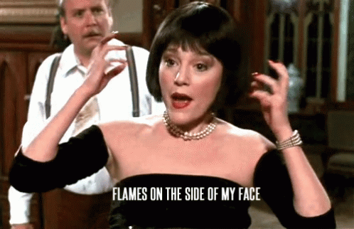 GIF of Madeline Khan as Mrs. White in Clue (1985), gesturing in frustration with her hands beside her head, saying "Flames on the side of my face!" 