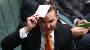 This is a photo of Australian MP Chris Bowen, current Minister of Climate Change & Energy.

He is a middle-aged white man in a black suit, with a white shirt & an orange tie holding a piece of paper over his head.