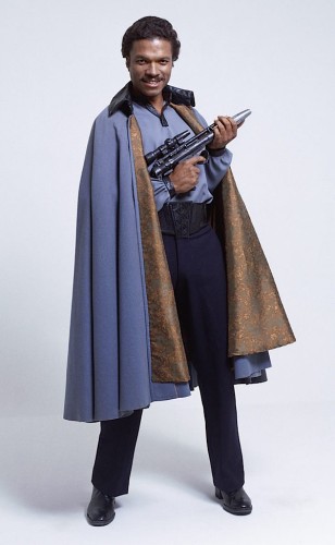 Lando Calrissian promo shot from the original Star Wars trilogy.  He is holding a blaster and wearing a cape and smiling like someone who has a blaster and a cape.