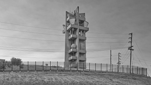 A concrete tower, with six platforms supporting large microwave antennas, on a hilltop behind a fence. 