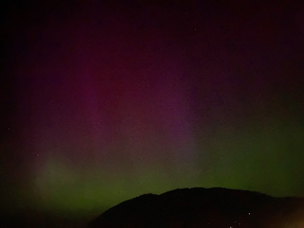 Red and green aurora borealis over the dark silhouette of a mountain