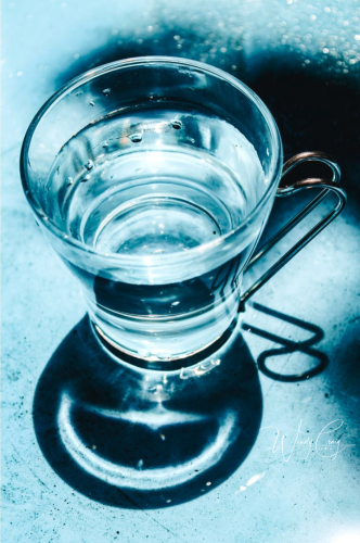 This is a photo of a glass espresso cup with a curled metal handle in dramatic light.