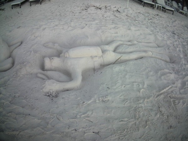a 3d sand sculpture of a scuba diver on a white sand beach
