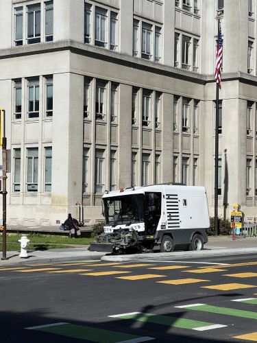A mini street sweeper in the Milvia Street protected bike lane, in front of City Hall. 