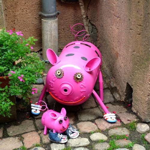Zwei Pink angemalte Gasflaschen mit Ohren Augen und Ringelschwanz, sehen aus wie kleine Schweinchen