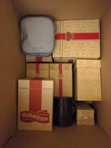 Photo d'un carton rempli de boites de la marque Franke & Heidecke, contenant des appareils photos Rolleiflex et accessoires pour lesdits appareils