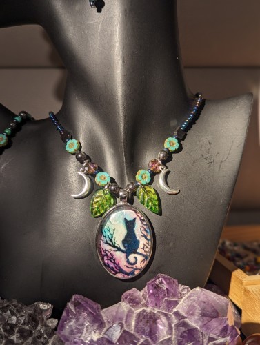 Handmade necklace with a black cat sitting on a tree branch and crescent moon with green purple skies necklace beaded with green leaf pendants and crescent silver moon pendants hematite styled beads czech crystal flower beads and colorful purple blue beads