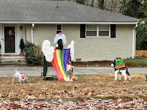 A holiday yard display featuring Santa dogs delivering gifts to an angel dog on a winged rainbow flag.