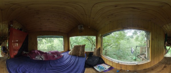 Panoramic view from inside the Mona tree house in Hambach Forest. You can see a large mattress with bed linen. The room is formed by three windows that are almost as large as the walls themselves. This gives you a comprehensive view of the treetops while lying in bed. The house was built in an oak tree 15 metres above the ground to protect the forest