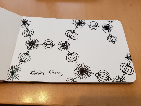 Hand drawn generative/iterative art in ink on an open page of my sketchbook. The abstract pattern is difficult to describe, but it looks a bit like an organic chemistry diagram with puff-balls and beads where the atoms would be.