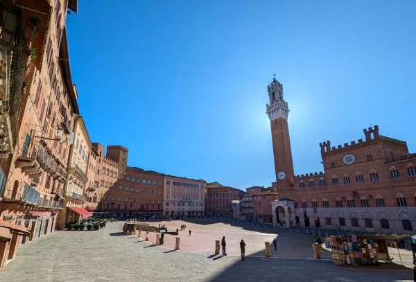 After a chilly night, the morning sun behind the Torre Del Mangia begins to heat-up the medieval Piazza del Campo at Siena, Tuscany, Italy. April 2024.
