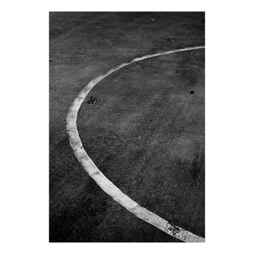Half frame 35mm high contrast black and white photo of a curved painted line on concrete. 