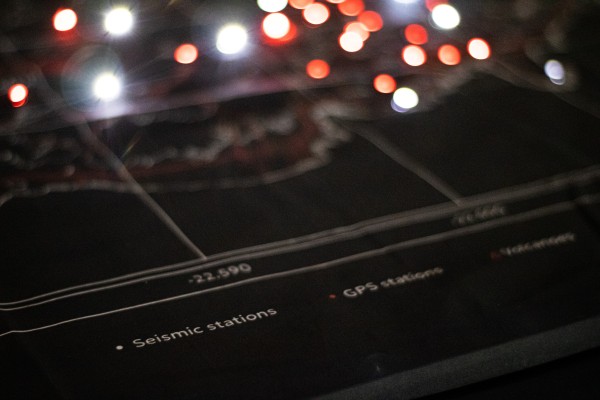 A black fabric displays a map of the Reykjanes peninsula. The legend at the bottom of the map reads, "white dot: seismic stations; red dot: GPS stations; triangle: volcanoes". A multitude of red and white LEDs are lit on the background.