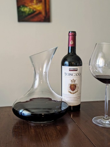 A decanter with red wine in it, next to a bottle of 2019 Kirkland signature Toscana