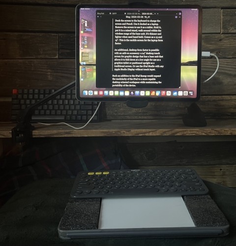 An iPad Pro is held in an adjustable stand attached to a shelf. Below it is a custom keyboard platform with a bluetooth keyboard and white Magic Trackpad.