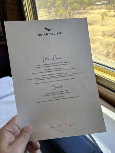 Menu being held up, with a view through a train window beyond. 