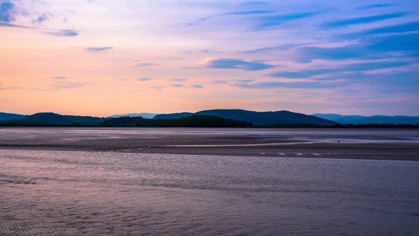 Rolling Hills of trees and blue at sun down with yellow and blue clouds in front of a estuary at low tide 