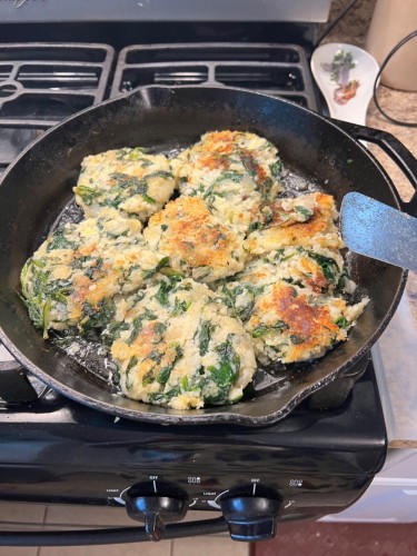 a large cast iron pan filled with 7 roundish potato and spinach patties