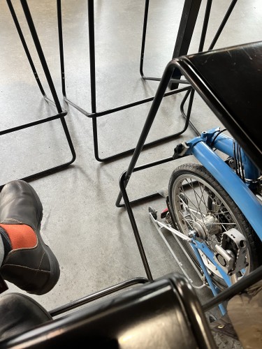Partial view of a shoe, metal chair legs, part of a folding bicycle