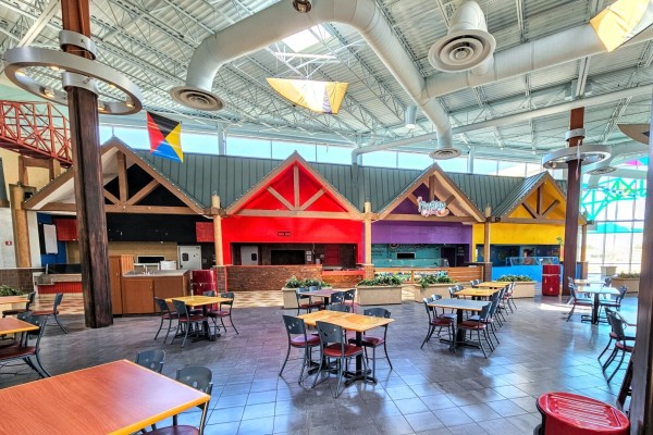 The only section of a shopping mall that isn't falling down and decaying rapidly is the food court area, where clean tables and chairs await customers that will never come. Along the wall, a row of barn-themed food stands in bright colors, but dark within, no longer selling their tasty delights. Very high ceilings have the ductwork of air circulation and heating/cooling vents, no longer in use, adding to the hot, stale, tomb like air.