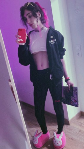 woman wearing a shit croptop, pink slippers, and black hoodie and pants, and handling a laptop in one hand