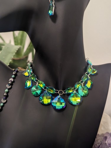 handmade green set with a green adjustable choker necklace with loads of glass green large and medium sized super shiny pendants
with fitting rhombic green earrings and beaded green and hematite styled bracelet
on a black doll with aloe plant behind it