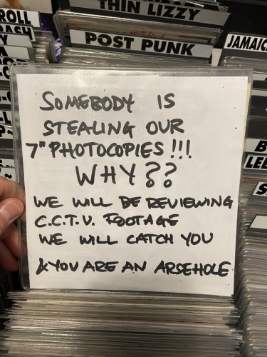 Photo of a hand written sign in a record sleeve that says - Somebody is stealing our 7 inch photocopies!!! WHY? We will be reviewing CCTV footage we will catch you and you are an arsehole 