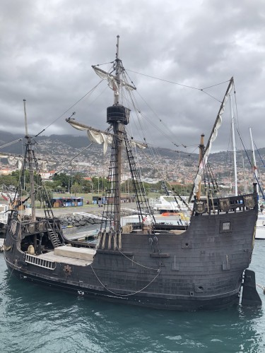 Replica wooden sailing ship moored in Funchal harbour with a dark cloudy sky behind it
