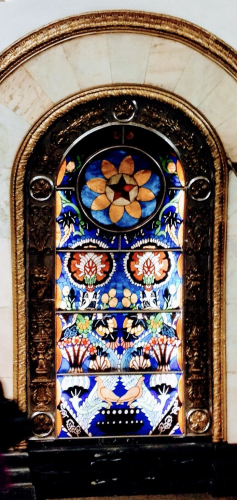 A multi colored stained glass window with several designs. Golden border arched around the window. 
