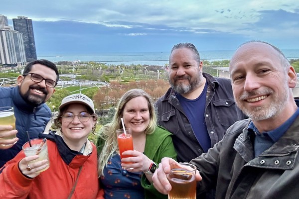 Andrés, Pauline, Michelle, Andrew & Rob smiling for a selfie, holding drinks, with a park and Lake Michigan in the background.